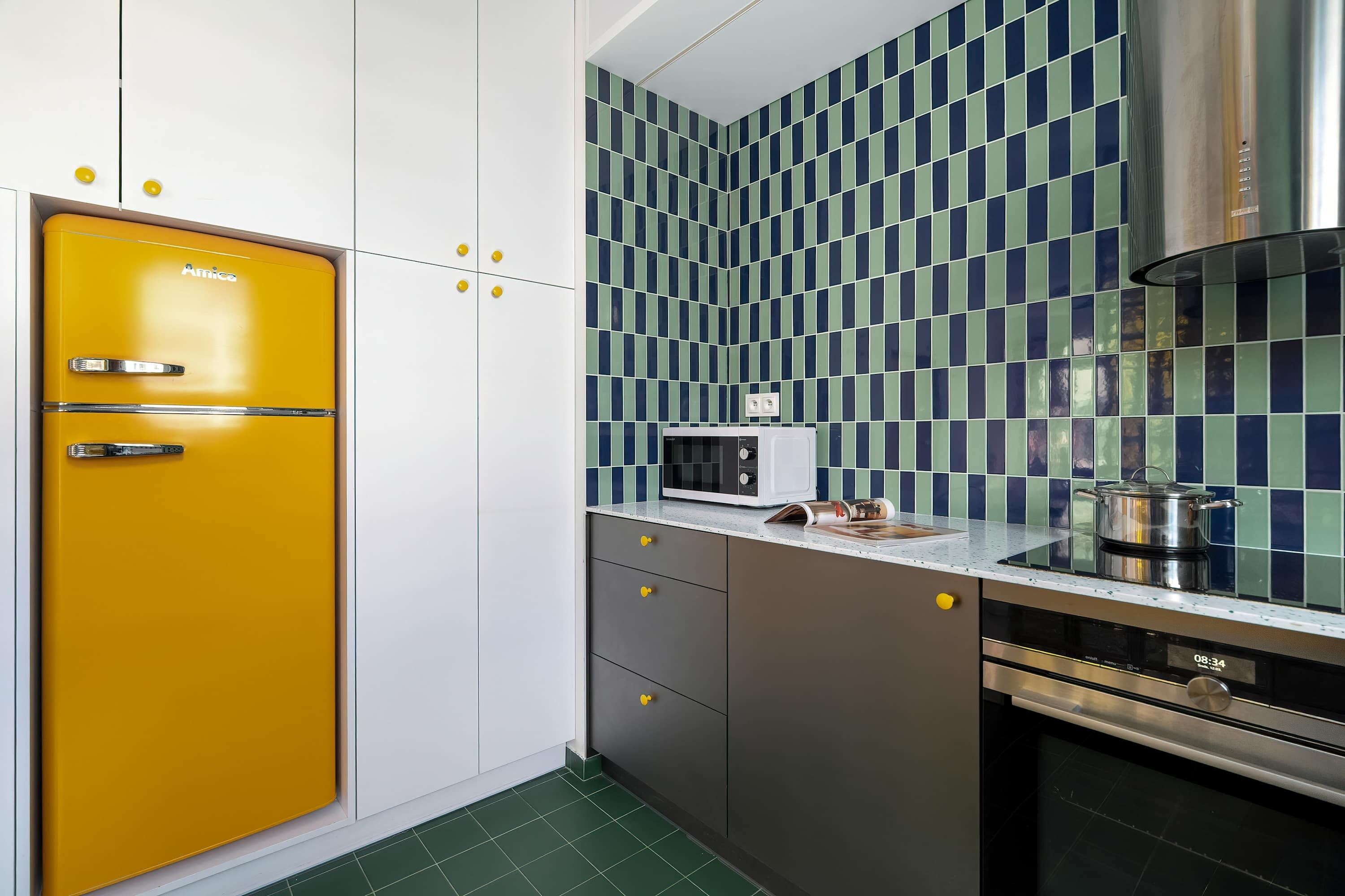 A kitchen with a yellow refrigerator, a microwave, and a stainless steel oven.