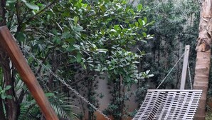 A hammock swing with a metal frame and a woven seat, set against a backdrop of dense foliage and a wall. - Studio Metrô Butantã (São Paulo)