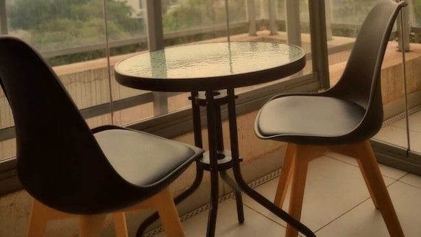 A balcony with a glass table and two chairs, overlooking a cityscape. - Studio Metrô Butantã (São Paulo)