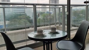 A balcony with a glass table and two chairs, overlooking a cityscape with buildings and trees. - Studio Metrô Butantã (São Paulo)