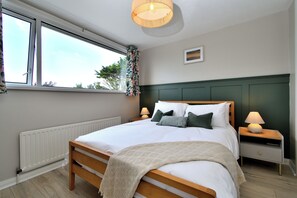 A bedroom with a bed, bedside lamps, a window with curtains, a radiator, and a picture on the wall. - Seven Glen Portrush: stylish coastal escape near the beach (Portrush)