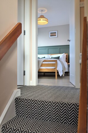 Ein Flur, der zu einem Schlafzimmer mit Bett, Kopfteil und Pendelleuchte führt.
