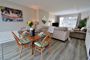 A modern living room with a dining area, featuring a sofa, a TV, and a painting on the wall. - Seven Glen Portrush: stylish coastal escape near the beach (Portrush)