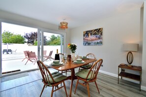 A dining area with a wooden table set for four, chairs with cushions, a vase with flowers, and a painting on the wall. - Seven Glen Portrush: stylish coastal escape near the beach (Portrush)