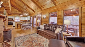 A cozy cabin interior with a wooden ceiling, a leather sofa, a dining table, and a kitchen area. - Log Cabin on 2 acres, hot tub, pond, fishing, pets, 1 mile TN Riverplace Venue (Chattanooga)