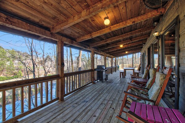 A covered outdoor deck with wooden railings, a grill, and seating. - Log Cabin on 2 acres, hot tub, pond, fishing, pets, 1 mile TN Riverplace Venue (Chattanooga)
