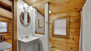 A wooden-paneled bathroom with a white sink, mirror, and toilet. - Log Cabin on 2 acres, hot tub, pond, fishing, pets, 1 mile TN Riverplace Venue (Chattanooga)