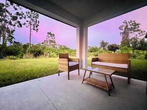 Un espace extérieur aménagé avec une terrasse en béton et des meubles en bois, entouré de verdure et d’arbres.