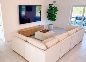 Ein modernes Wohnzimmer mit einem großen Ecksofa, einem flachbildfernseher an der Wand, einem Holzkonsole und einem Topfpflanzen.
