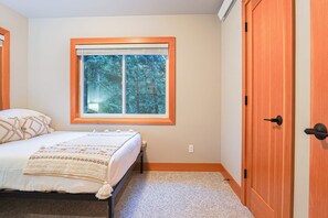 Ein Schlafzimmer mit einem Bett, einem Fenster mit Blick auf Bäume und einer Holztür.