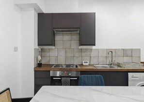 A modern kitchen with dark cabinets, a stainless steel stove, and a dishwasher. - Long stays - London 2 Bed Apartment - Free Parking & WIFI (London)