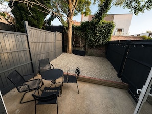 An outdoor patio with a round table and four chairs, surrounded by a gravel area and a wooden fence. - Long stays - London 2 Bed Apartment - Free Parking & WIFI (London)