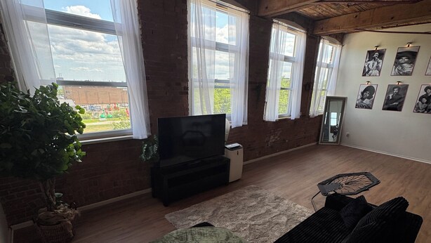 Ein Wohnzimmer mit einer Couch, einem Fernseher und einem großen Fenster mit Vorhängen.