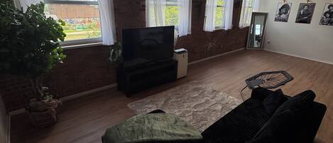 Una sala de estar con sofá, televisión y un ventanal con cortinas.