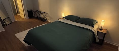 A bedroom with a bed, two bedside lamps, a hanging light fixture, a door, and a small table with a lamp.