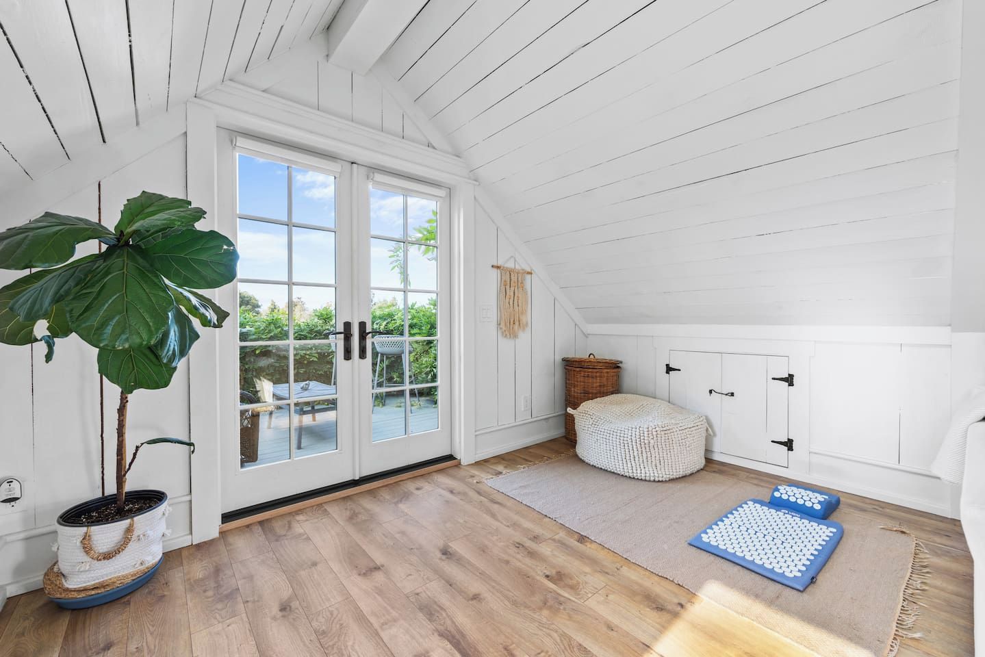 A room with a large window, a potted plant, a woven pouf, and exercise mats.