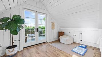 A room with a large window, a potted plant, a woven pouf, and exercise mats.