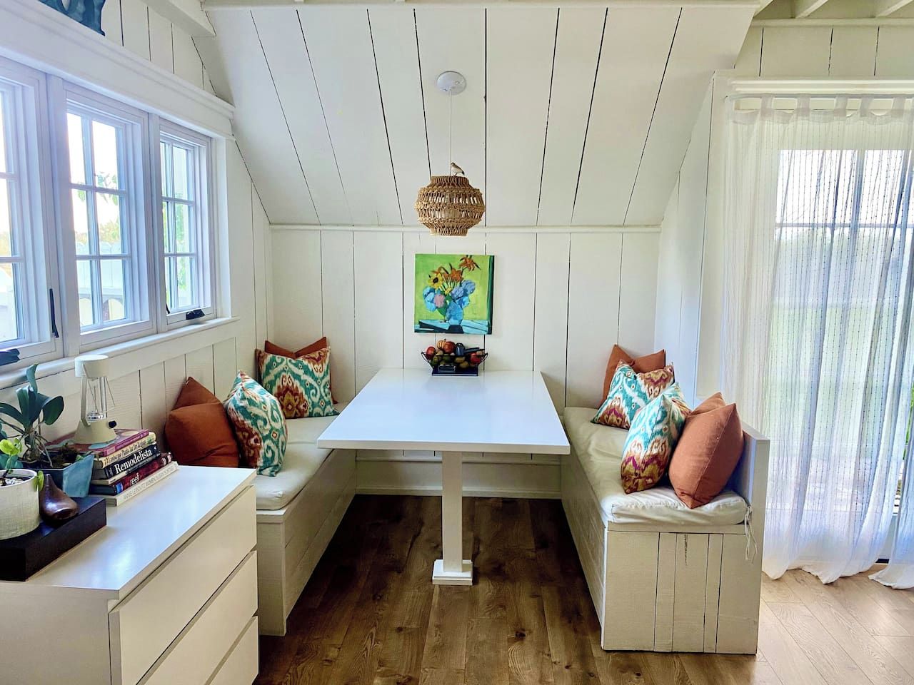 A cozy room with a white table, bench seating, and a painting above the table.