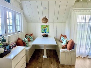 A cozy room with a white table, bench seating, and a painting above the table.