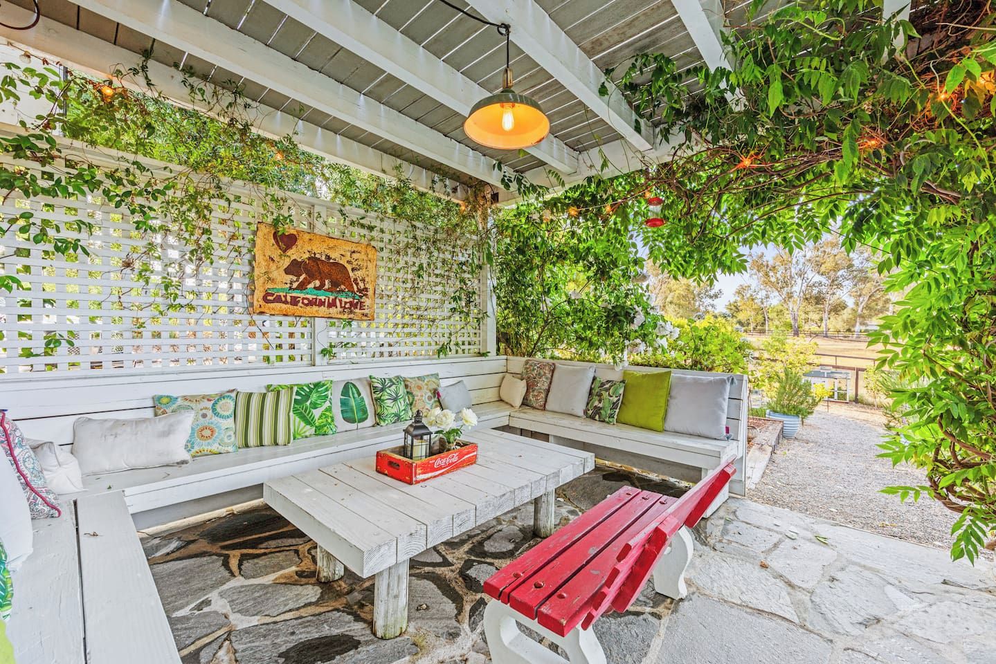 Espaço ao ar livre com bancos e mesa de madeira, rodeado por vegetação e um muro decorativo.