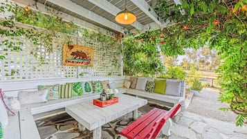Espaço ao ar livre com bancos e mesa de madeira, rodeado por vegetação e um muro decorativo.