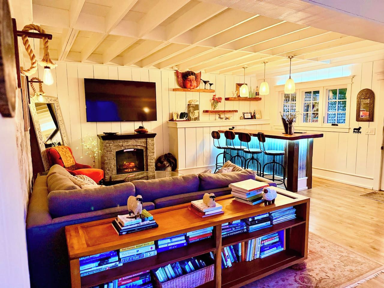Un salon chaleureux avec une cheminée, un grand téléviseur à écran plat, un canapé et une table basse agrémentée de livres et d’objets décoratifs.