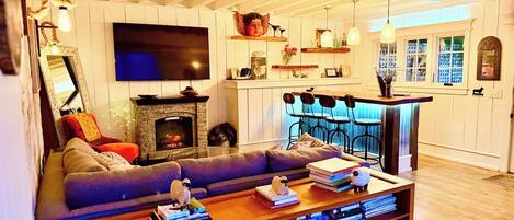 A cozy living room with a fireplace, a large flat-screen TV, a sofa, and a coffee table with books and decorative items.