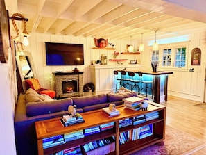 A cozy living room with a fireplace, a large flat-screen TV, a sofa, and a coffee table with books and decorative items.