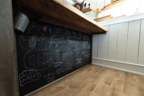 A room with a blackboard filled with handwritten notes and drawings, wooden flooring, and a white wall with a shelf above.