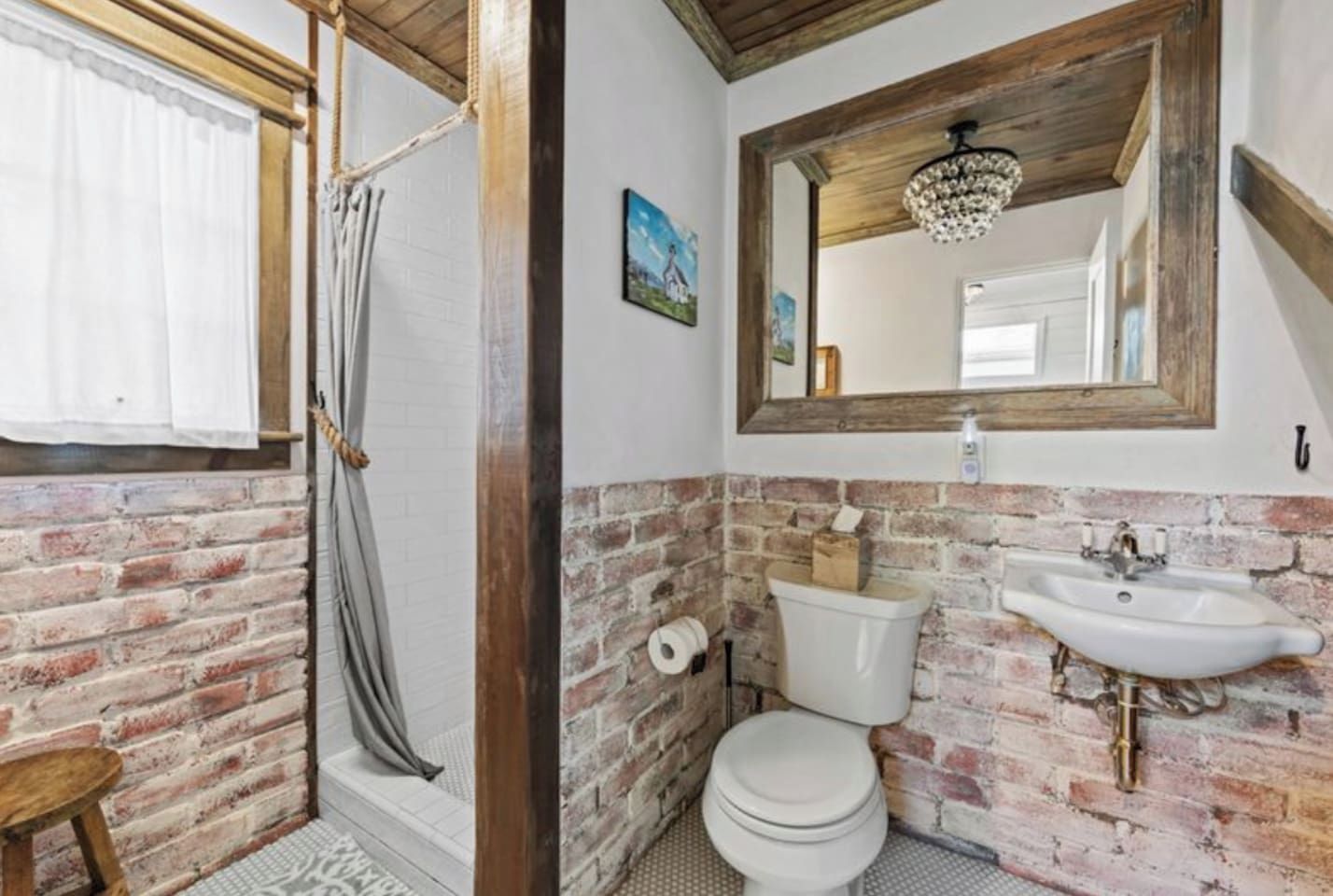 A bathroom with a brick wall, a white toilet, a sink with a mirror above it, and a shower curtain.