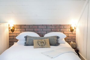 Ein Bett mit weißer Bettwäsche, zwei Kissen und einer Decke. An beiden Seiten des Bettes befinden sich zwei Wandlampen.