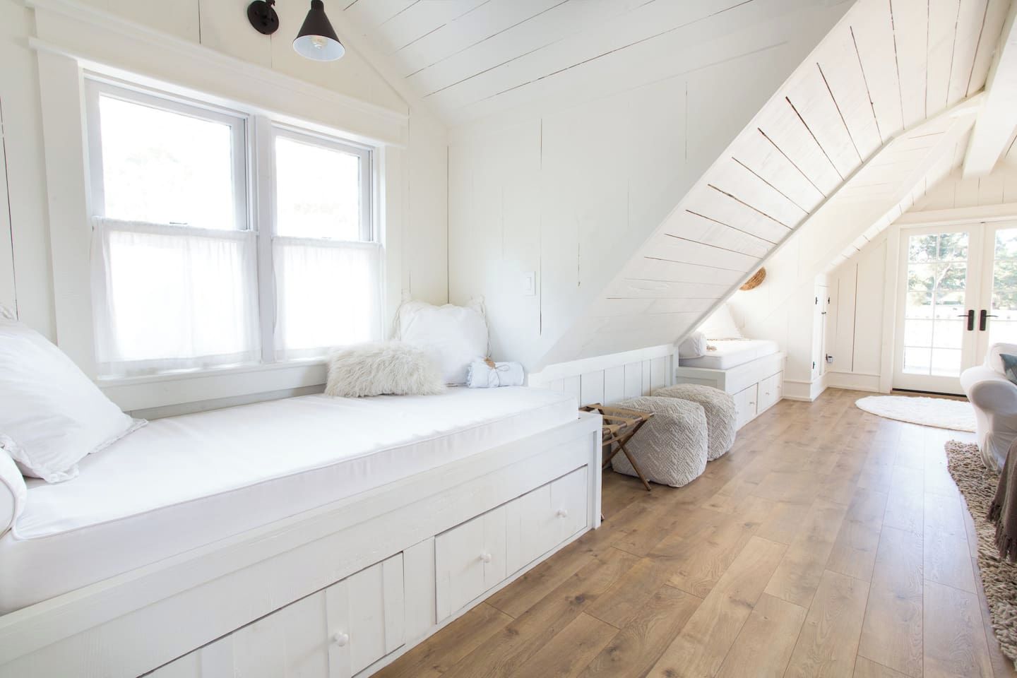 Una habitación con un banco empotrado junto a la ventana, un espacio para dormir elevado y suelo de madera.