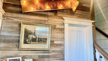 A rustic interior with a wooden wall, a framed historical photograph, a directional sign, and a staircase.