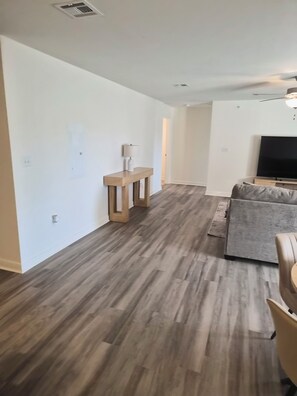 Un salón espacioso con piso de madera, un sofá gris, una consola de madera y un televisor de pantalla plana.