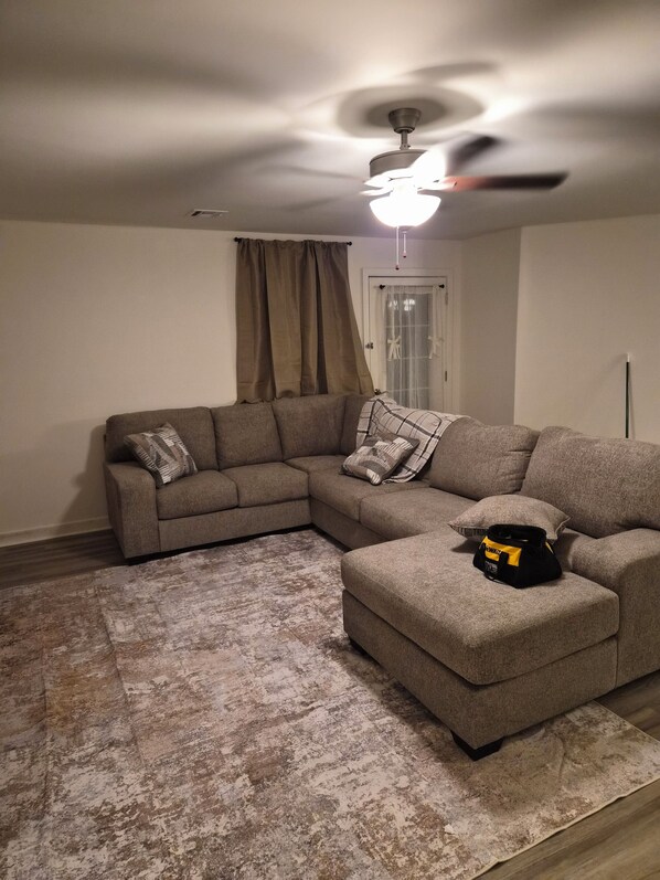 Una sala de estar con un sofá modular, un ventilador de techo y una alfombra estampada.