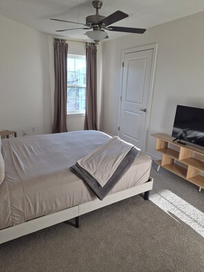 Habitación de hotel con cama, ventilador de techo, televisor sobre un soporte de madera y una puerta.