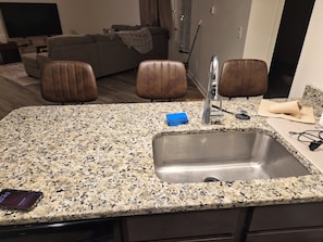 Cocina con encimera de granito, pileta de acero inoxidable y sillas de cuero marrón.