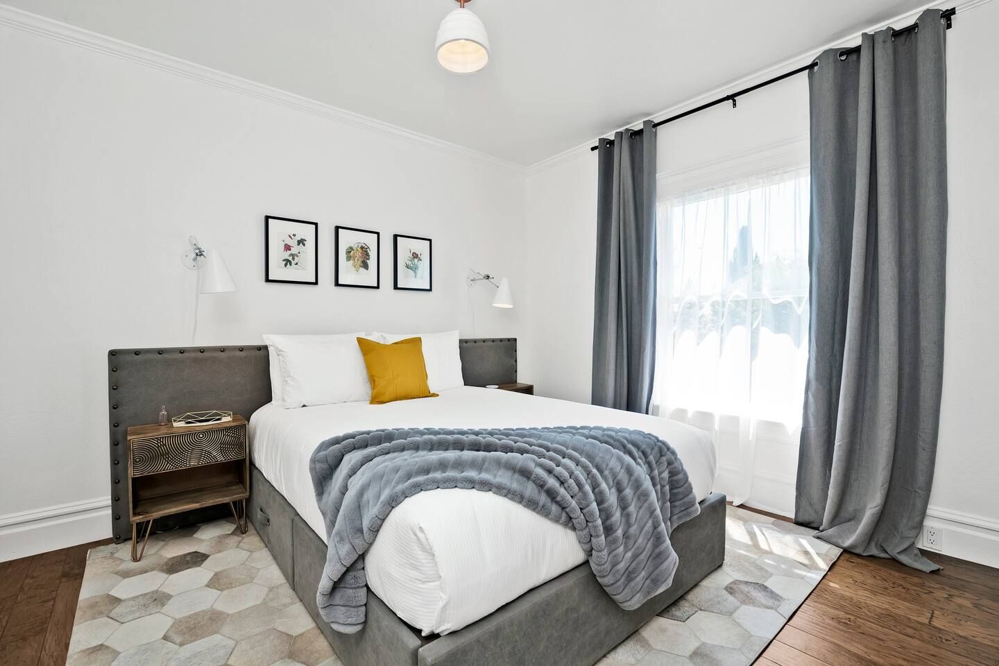 Quarto moderno com uma cama grande, cortinas cinzas e vista para a cidade.