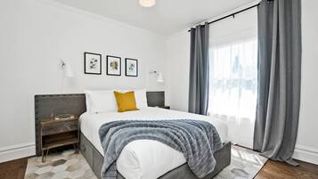 Quarto moderno com uma cama grande, cortinas cinzas e vista para a cidade.