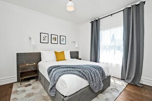 Un dormitorio moderno con una cama grande, cortinas grises y vistas a la ciudad.