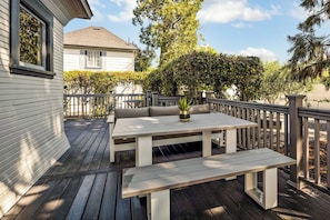 Una terraza con una mesa y bancos, rodeada por una barandilla de madera y follaje.