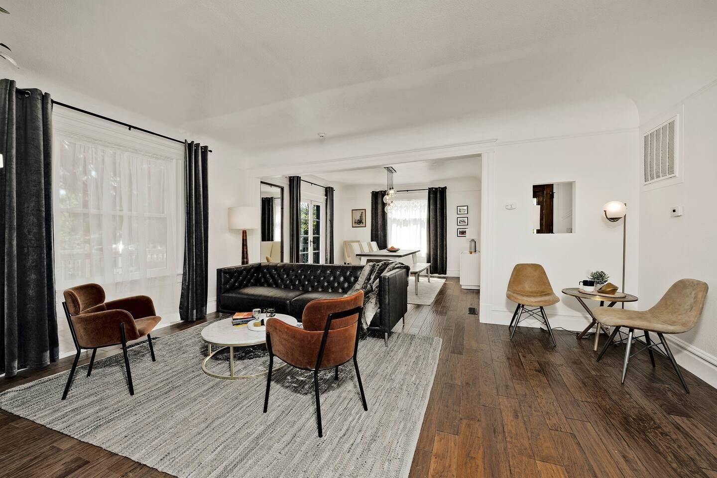 Een moderne woonkamer met een hoekbank, twee fauteuils, een salontafel en een eethoek met een tafel en stoelen.
