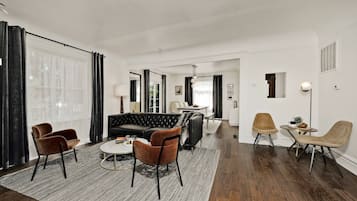 Een moderne woonkamer met een hoekbank, twee fauteuils, een salontafel en een eethoek met een tafel en stoelen.
