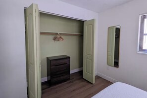 A bedroom with a bed, a dresser, a closet with a mirror, and a window with blinds.