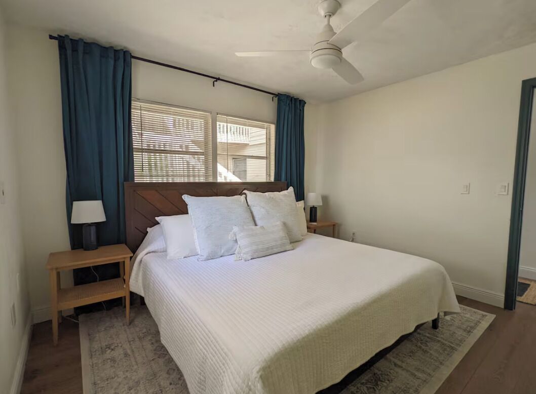 Ein Schlafzimmer mit einem Bett, zwei Nachttischen, einem Deckenventilator und einem Fenster mit Vorhängen.