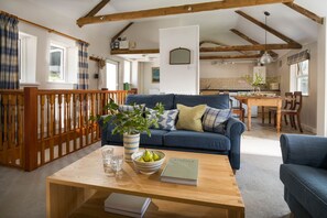 A cozy living room with a blue sofa, wooden coffee table, and a dining area with a wooden table and chairs. - Marigold Cottage - sleeps 4 guests  in 2 bedrooms (Port Gaverne)