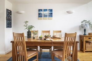 A dining area with a wooden table, six chairs, and a blue rug. - Mulberry Eco Beach House - sleeps 6 guests  in 3 bedrooms (Porthtowan)