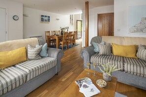 A living room with two sofas, a coffee table, and a dining area with chairs and a table. - Mulberry Eco Beach House - sleeps 6 guests  in 3 bedrooms (Porthtowan)