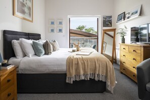 A bedroom with a bed, bedside tables, a dresser, a TV, and framed pictures on the wall. - Mulberry Eco Beach House - sleeps 6 guests  in 3 bedrooms (Porthtowan)