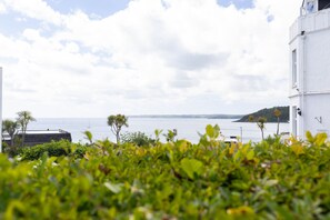 A coastal view with a building, a body of water, and a distant island. - Ocean Waves Apartment - sleeps 4 guests  in 2 bedrooms (Falmouth)